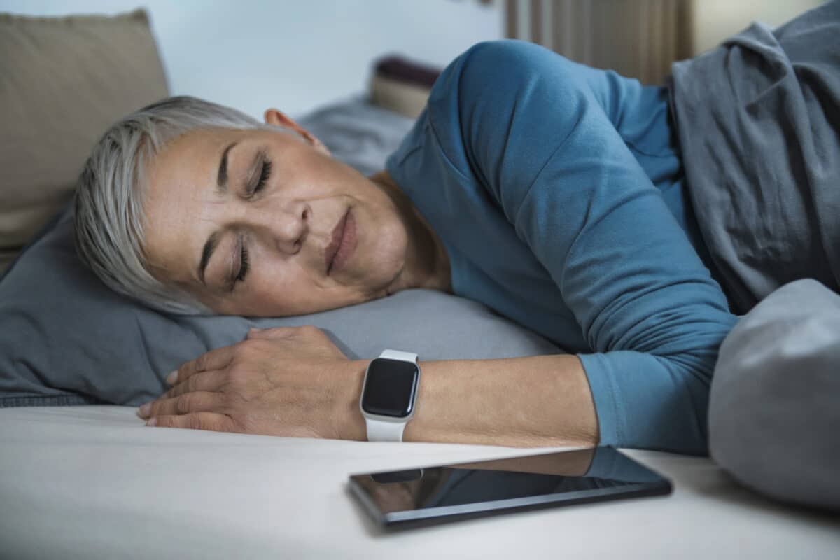 Sleep Apps - Tech-savvy Senior Woman Sleeping in Bed, Using Smart Phone and Smart Watch to Improve her Sleeping Habits