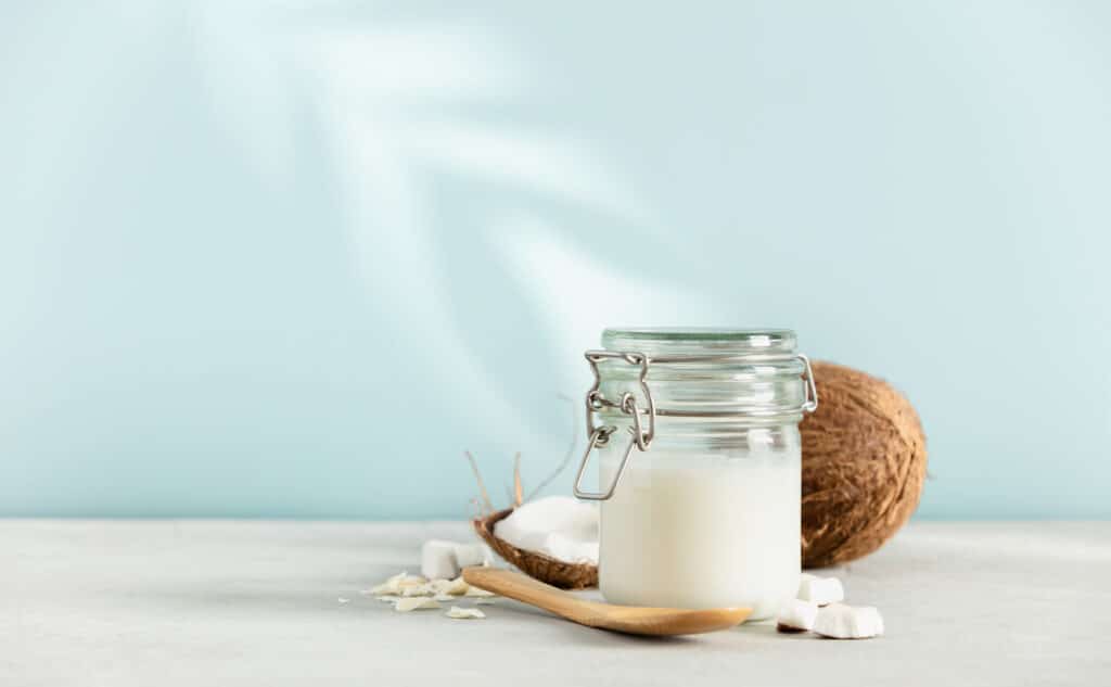 Coconut oil in jar with fresh coconut and tropical leaf shadow on blue background, Spa cosmetic and food ingredient, space for text