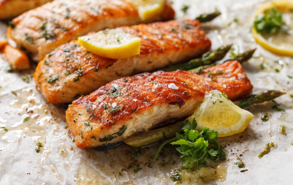 Baked salmon fillet with aromatic herbs and lemon on baking paper close up view