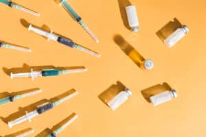 Syringes are filled with injection and medical vaccine bottles on a yellow background. Flat lay