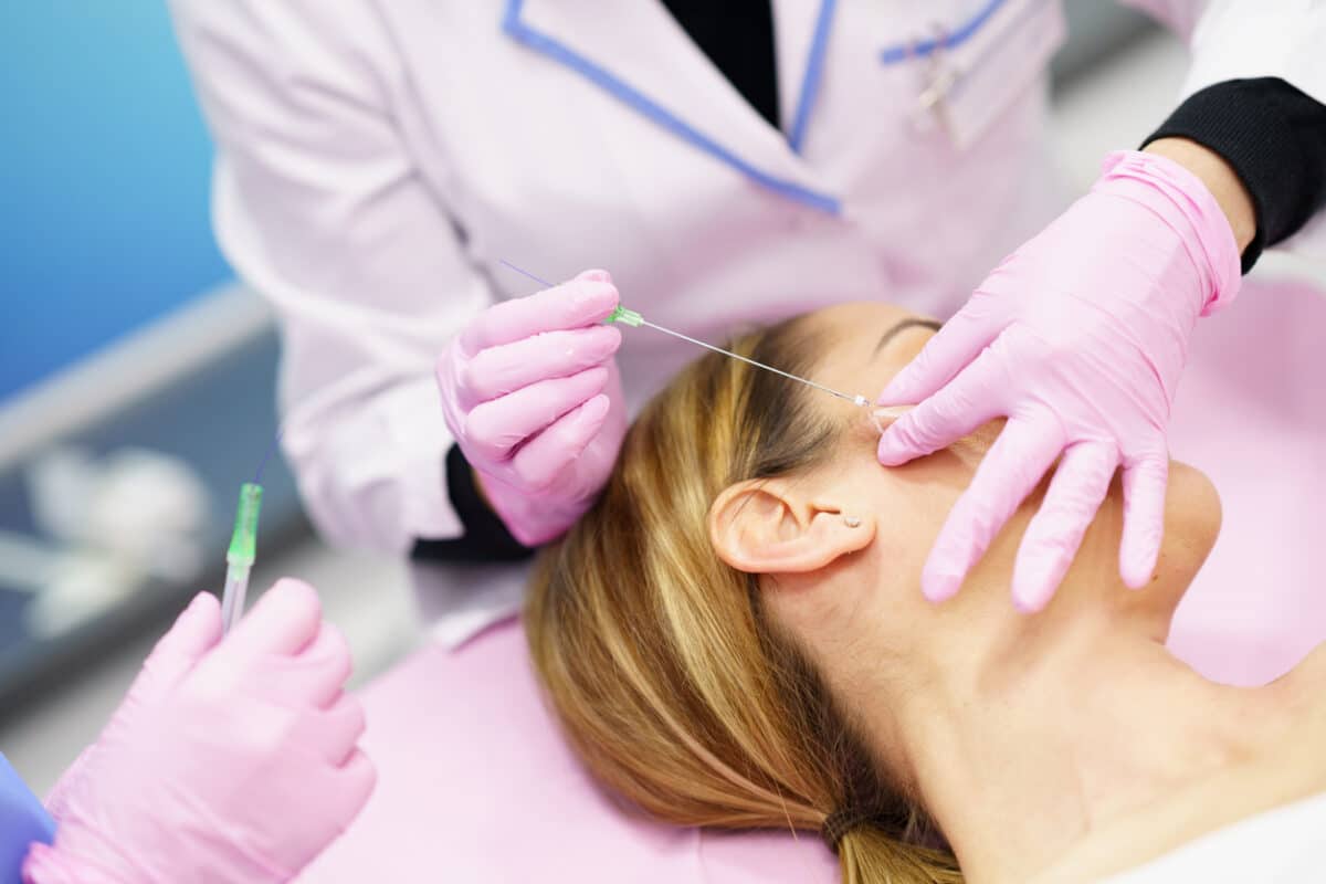 Doctor injecting PDO suture treatment threads into the face of a middle-aged woman.