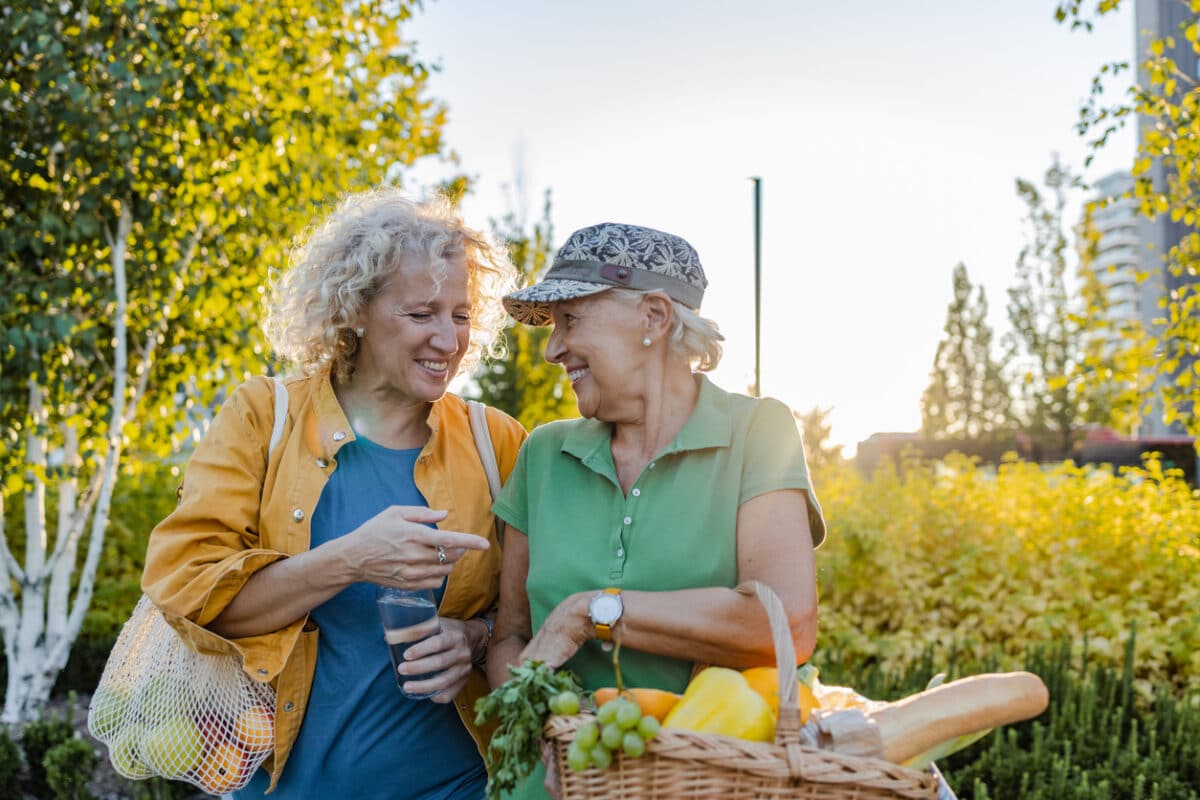 Portrait of two housewives coming back from supermarket. Smiling women are carrying fruits and vegetables.