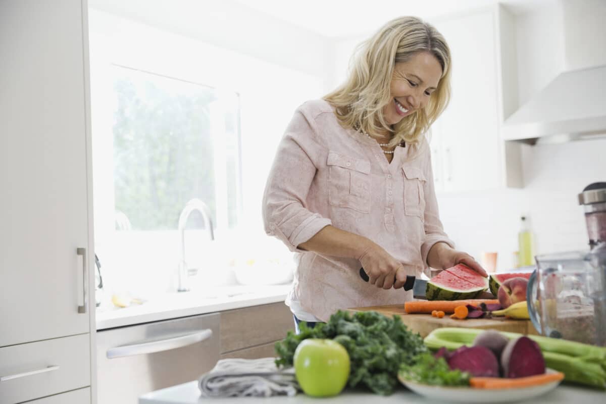 Happy woman cutting watermelon at kitchen counter
