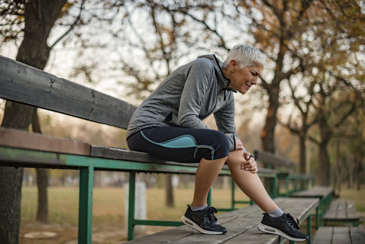 Image of Senior Woman Runner Hold Her Sports Injured Knee Outdoor. Injury From Workout Concept. Mature Woman Suffering From an Knee Injury While Exercising and Running