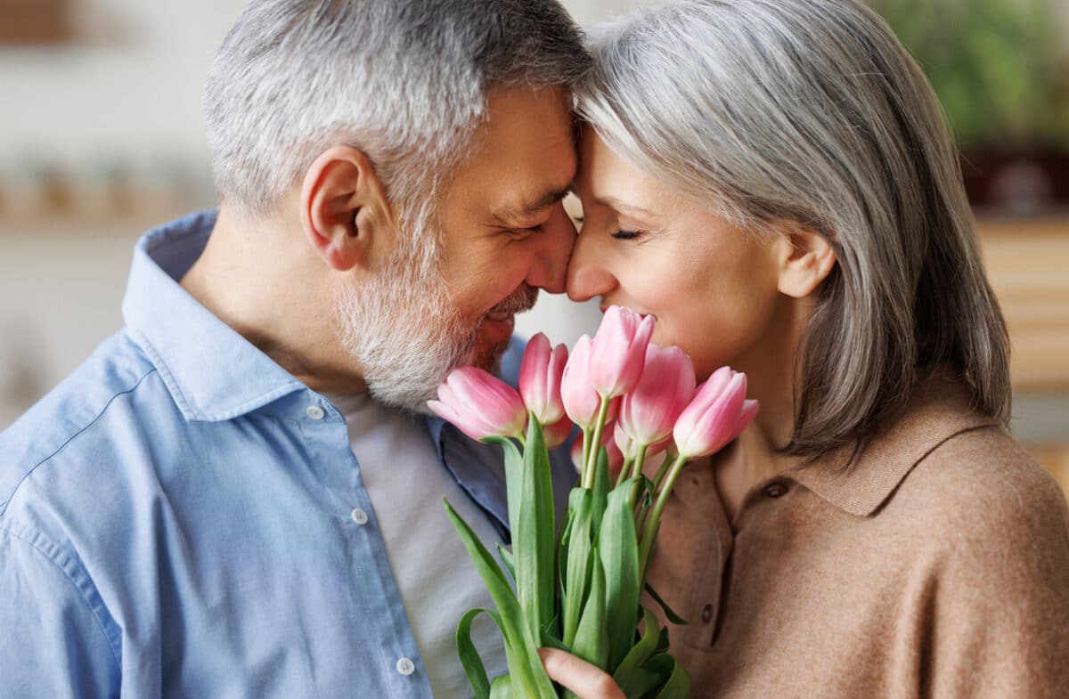 Elderly couple in love hugging on Valentine's day. A loving senior husband gives his wife a tender bouquet of tulip flowers