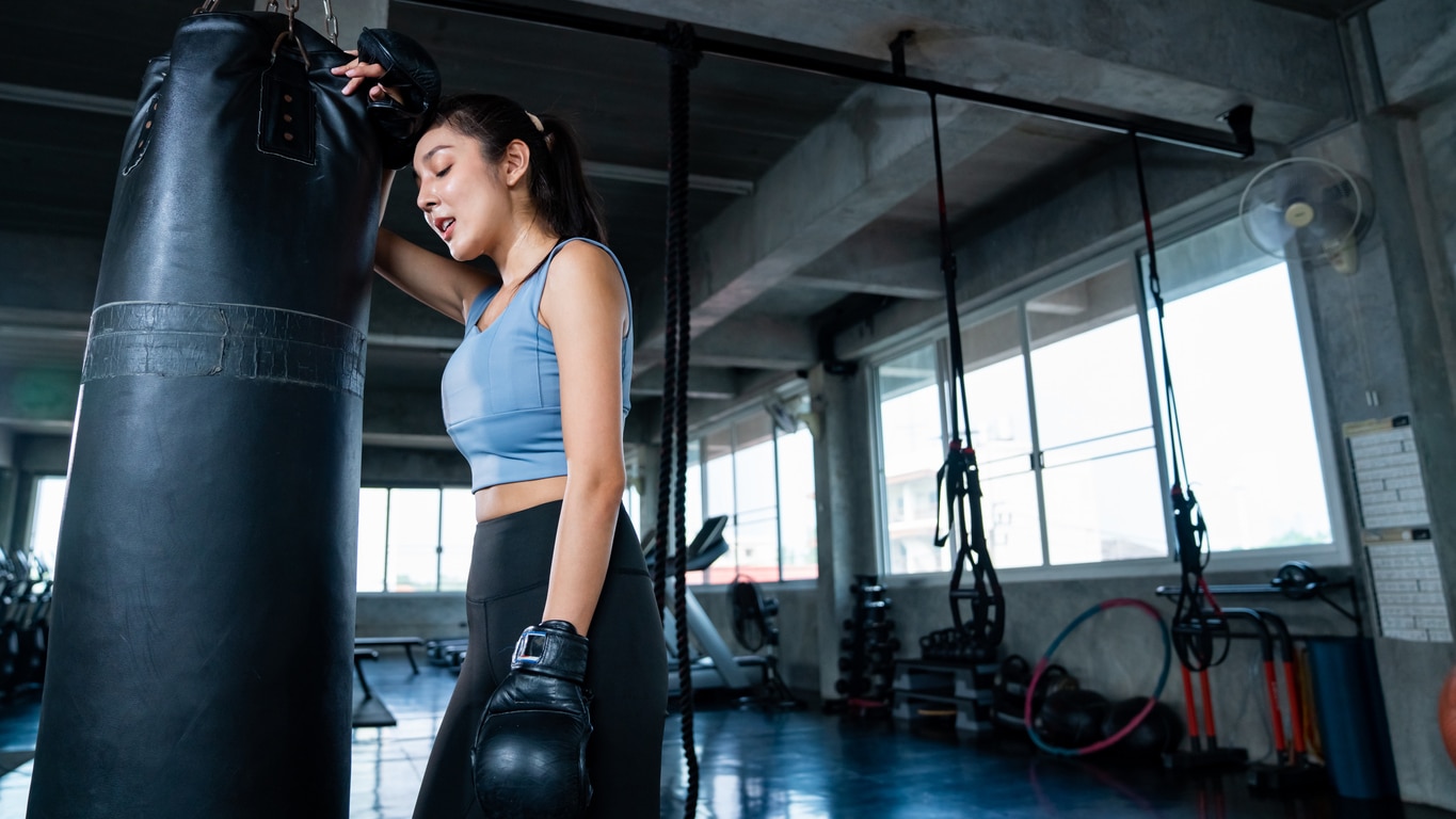 Strong Asian athletic woman in sportswear wearing boxing gloves do workout exercise punching boxing bag at fitness gym. Healthy fit and firm female do sport training and bodybuilding at sport club.