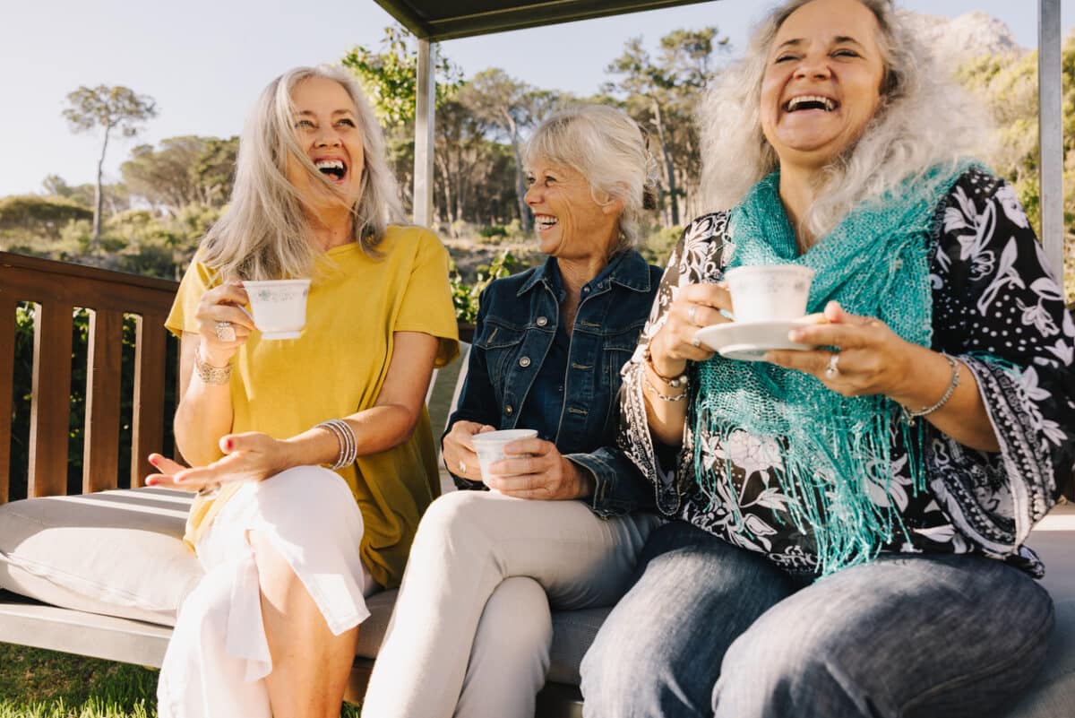 Senior women laughing happily while having tea together. Group of elderly friends enjoying their summer vacation at a spa resort. Three mature women enjoying themselves after retirement.
