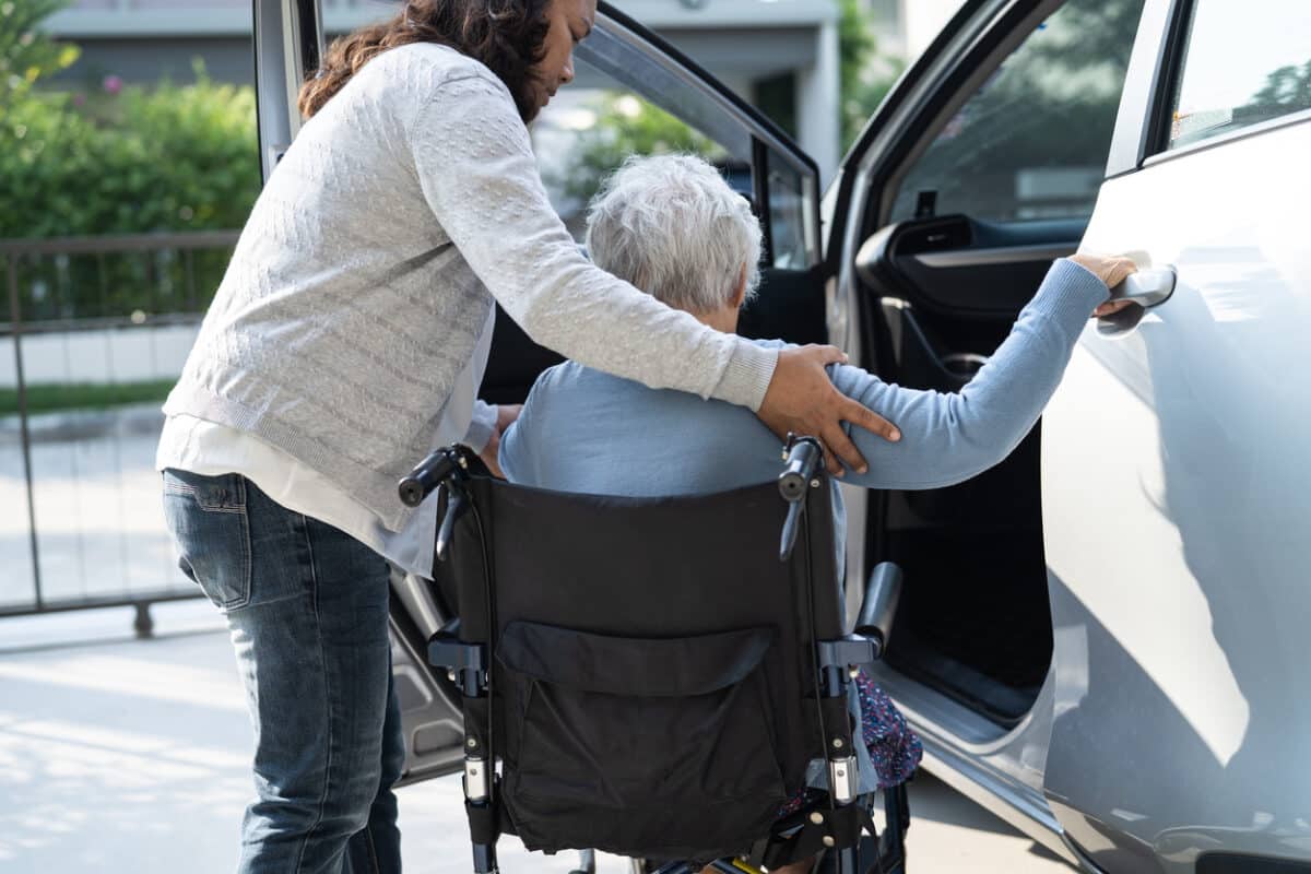 Older woman getting in a car from a wheelchair with assistance