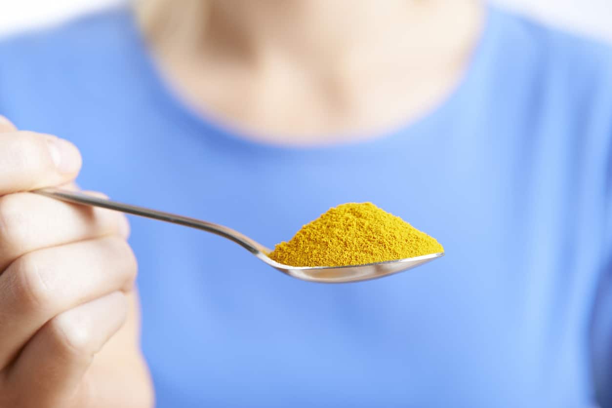 Woman With Spoonful Of Tumeric Powder