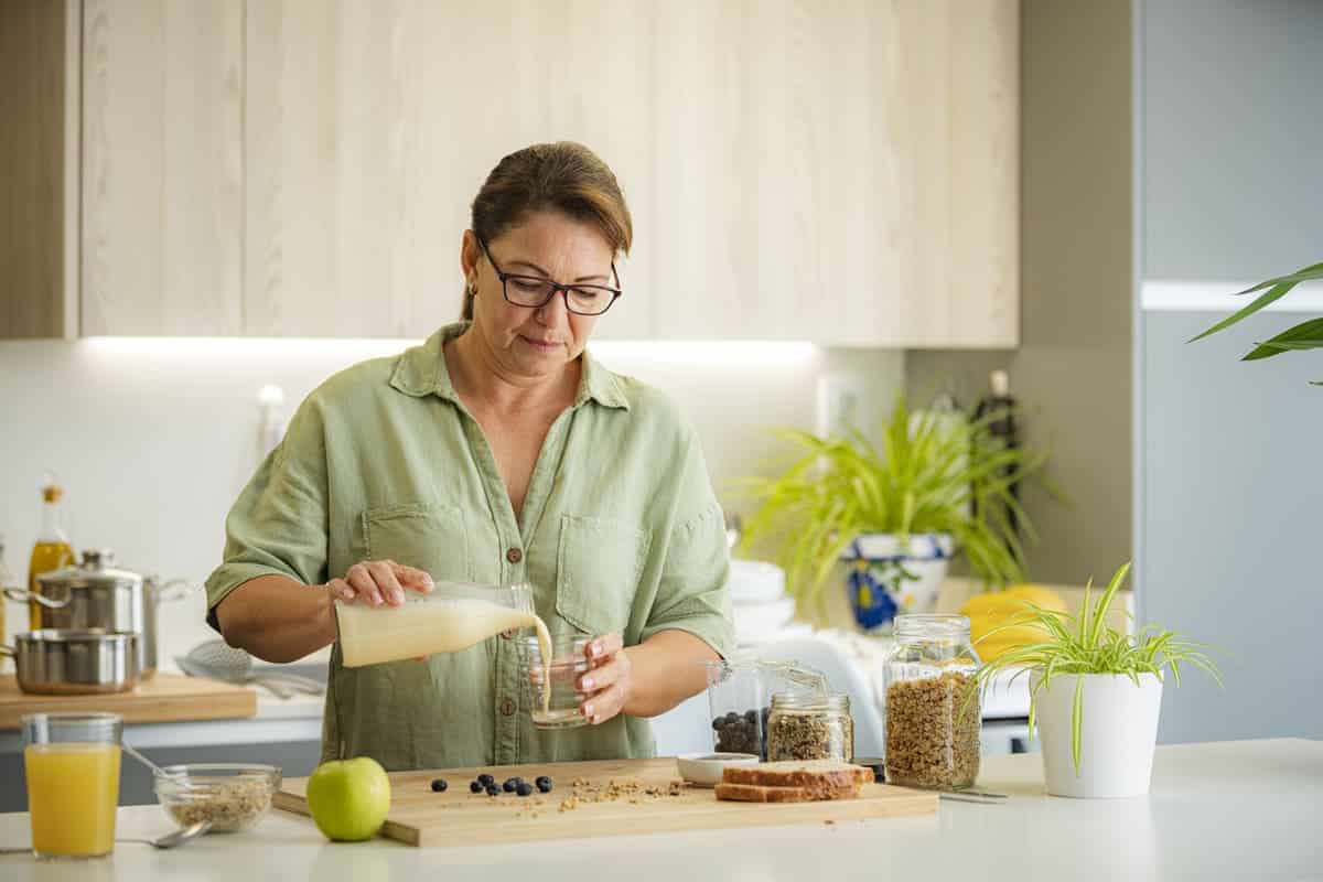 woman pouring vegan milk or almond milk into a glass