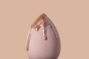 Closeup photography of beauty blender with dripping bronzer on it.Neutral beige background,large banner with copy space. Bronzing Drops to Glow Up Your Foundation