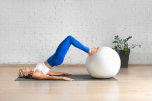 Workout with fitness ball. Fit Caucasian woman practice hamstring roll-in using props in loft studio indoor. Lower Body Exercise Without Lunges or Squats