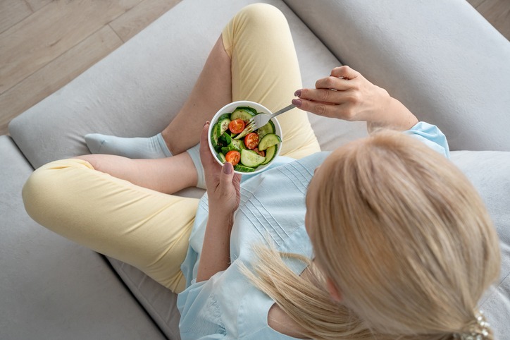 Woman preparing and eating a healthy salad in a modern kitchen with fresh ingredients on the counter. Metabolism Mistake for Women Over 50 cutting calories