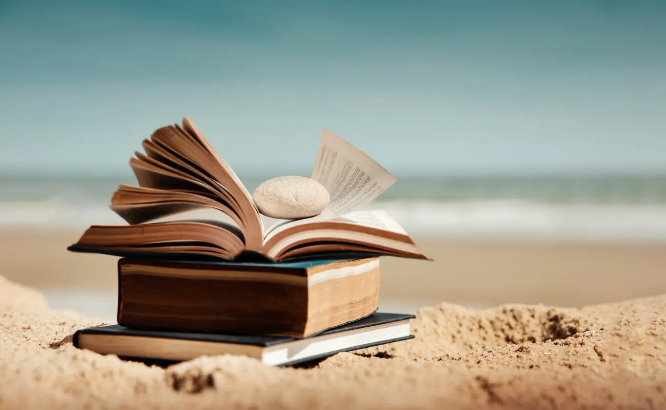 Open book placed on sandy beach with ocean background. Concept of reading, learning, education, relaxation and personal growth through books. Sandy's Selections: 5 Books for July